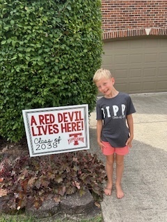 Kindergarten student standing with the yard signing saying A Red Devil Lives Here!