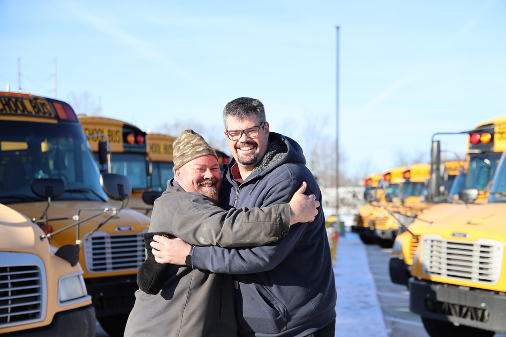 Lead mechanic and director of transportation get silly and hug each other at the new bus parking lot.  