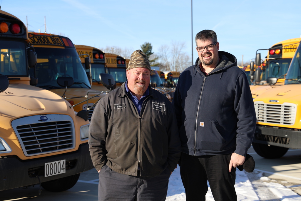 Director of Transportation and Lead Mechanic pose in front of the buses parked in the new parking lot.  