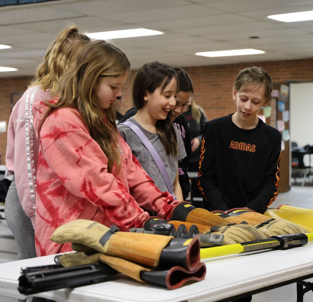 Students look at and touch gloves worn by linemen.