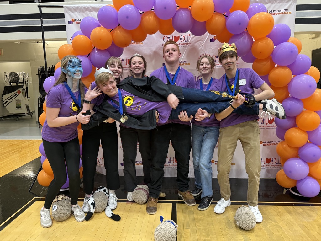 high school students smiling in front of orange and purple balloon arch, dressed as characters