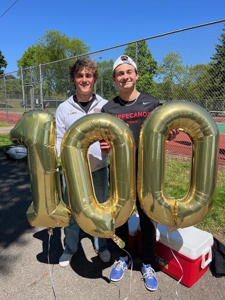 THS tennis player stands with balloons with the number 1-0-0 to celebrate 100 tennis match wins.