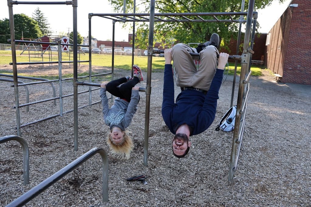 A dad and his daughter hang upside down on the monkey bars.