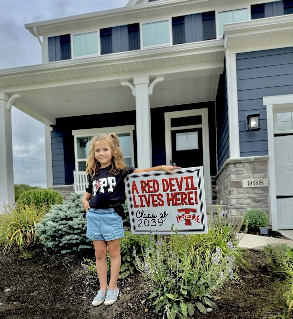 A kindergarten student with a yard sign, Class of 2039, to welcome them to school.