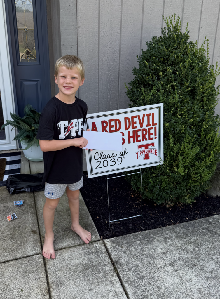 A kindergarten student with a yard sign, Class of 2039, to welcome them to school.