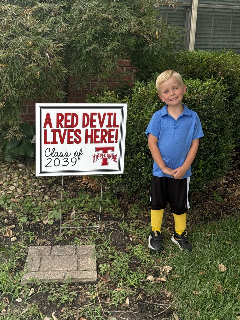 A kindergarten student with a yard sign, Class of 2039, to welcome them to school.