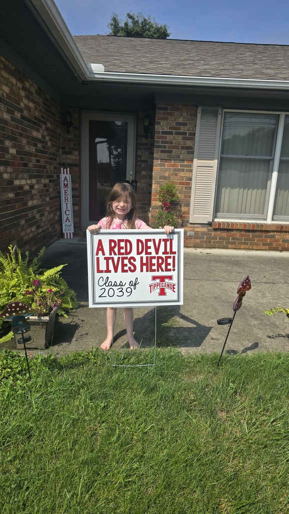 A kindergarten student with a yard sign, Class of 2039, to welcome them to school.