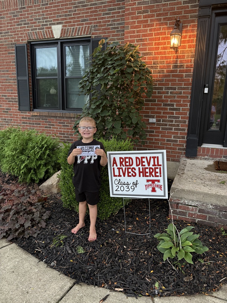 A kindergarten student with a yard sign, Class of 2039, to welcome them to school.