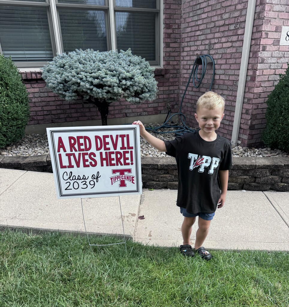 A kindergarten student with a yard sign, Class of 2039, to welcome them to school.