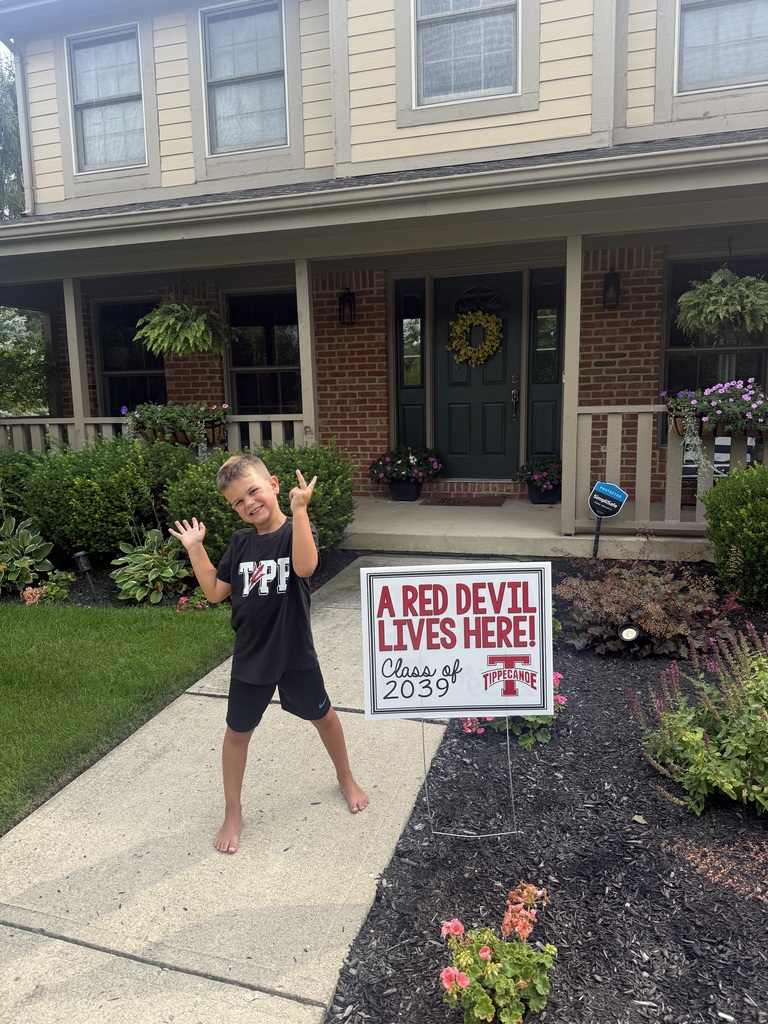 A kindergarten student with a yard sign, Class of 2039, to welcome them to school.