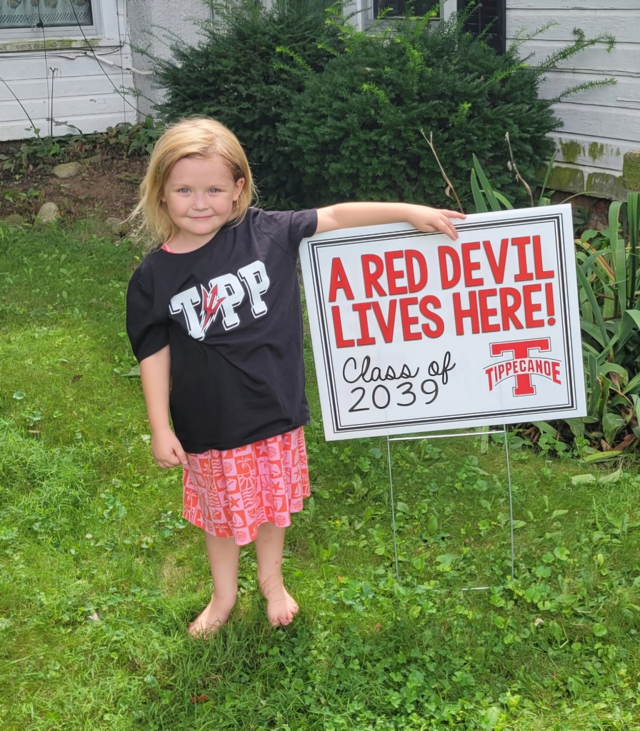 A kindergarten student with a yard sign, Class of 2039, to welcome them to school.