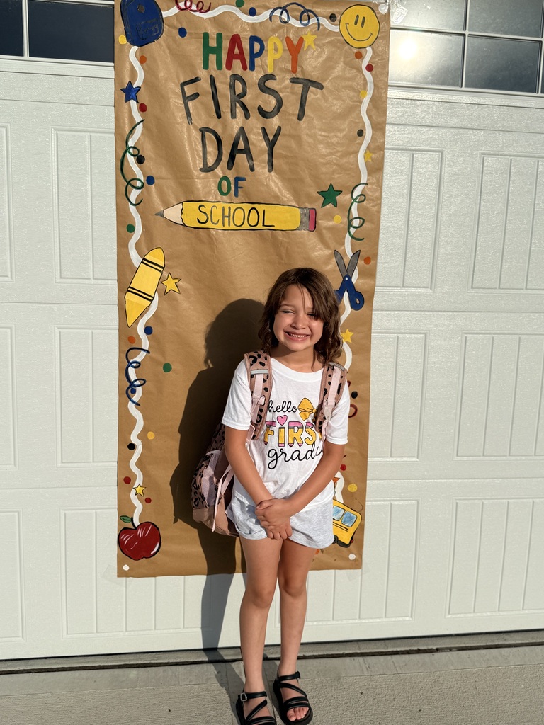 A first grader poses in front of a sign that says Happy First Day of School.