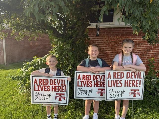 Three elementary students pose for a picture with their Red Devils class signs.