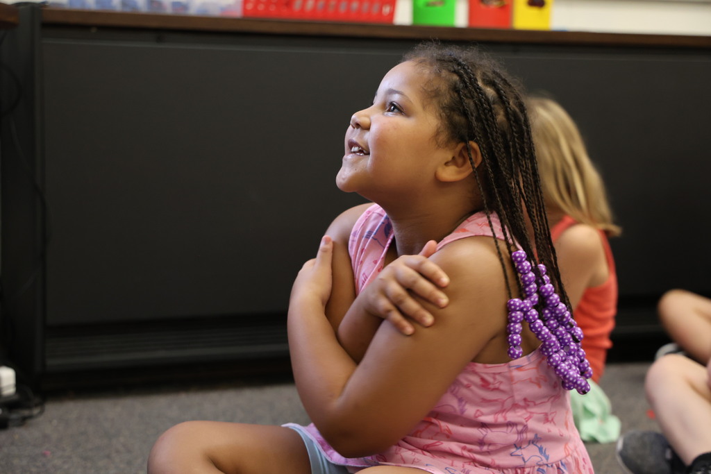 A student gives herself a big hug during story time as she acts out the pages of The Book of Rules.