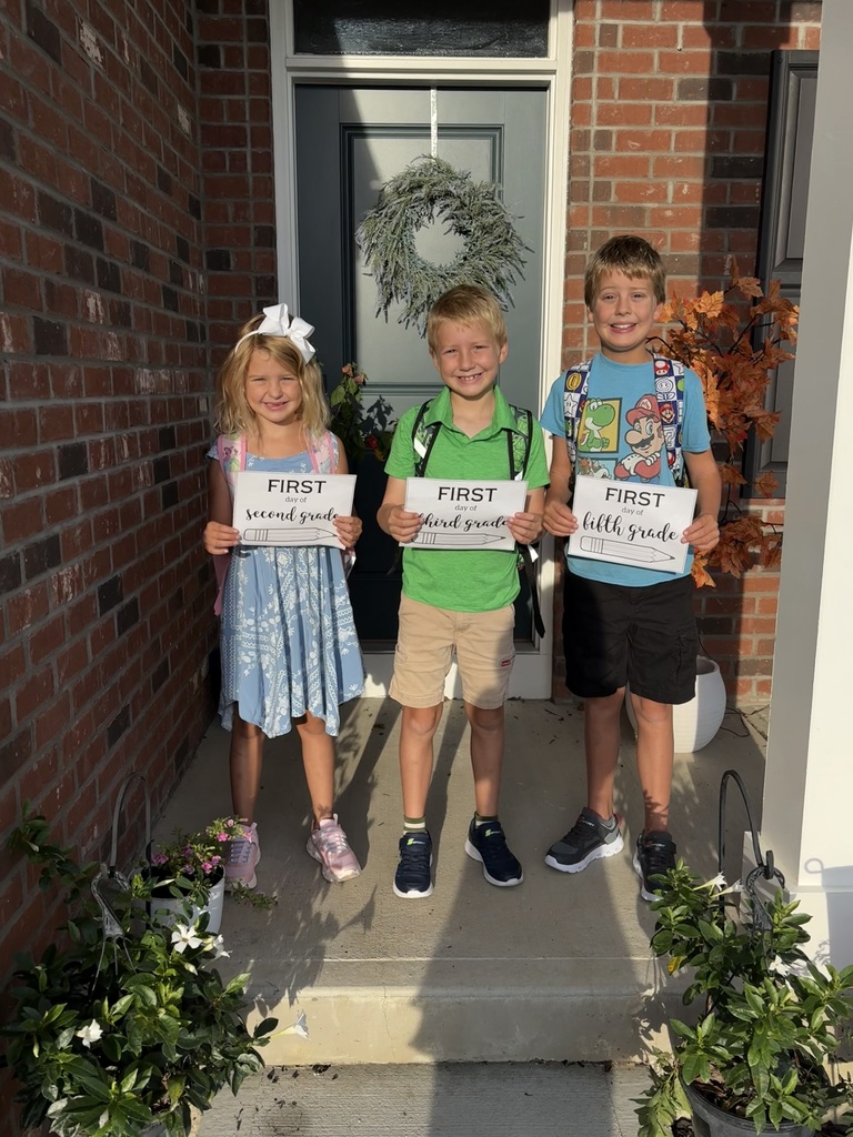 Siblings pose for a first day of school picture in front of their house.