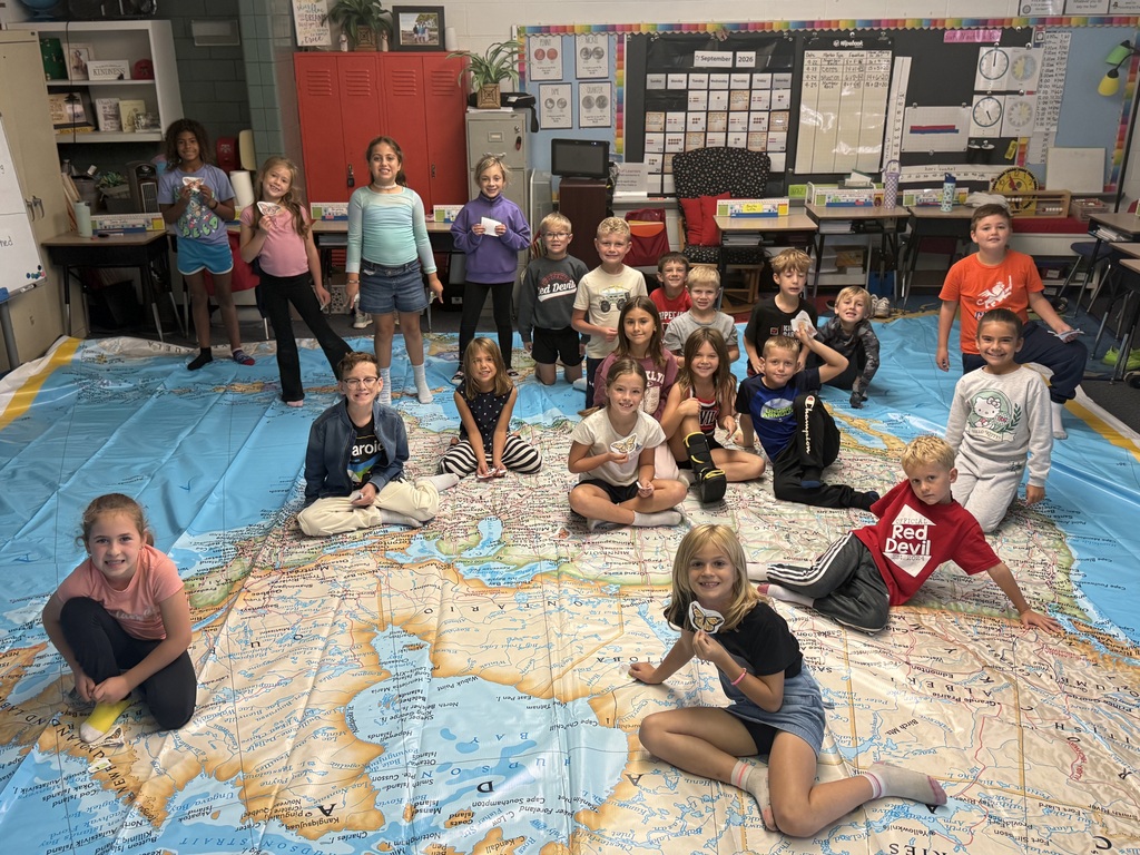 Students sit on a world map holding their butterflies that will migrate.