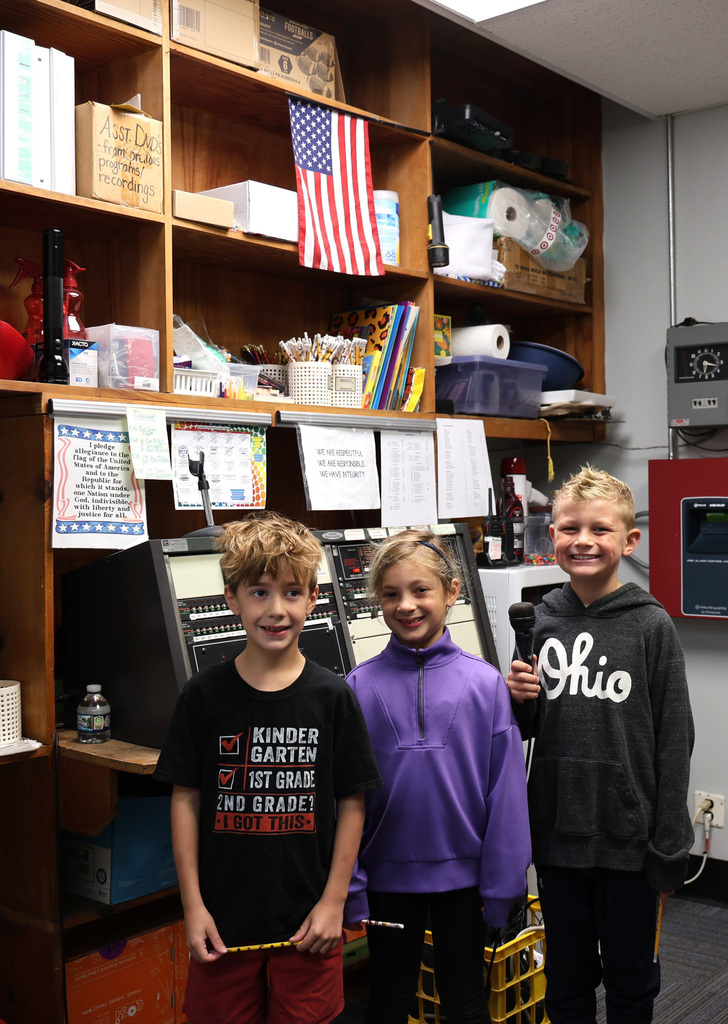 Three students at Broadway stand together under the American Flag after saying the Pledge of Allegiance during the school's morning announcements.