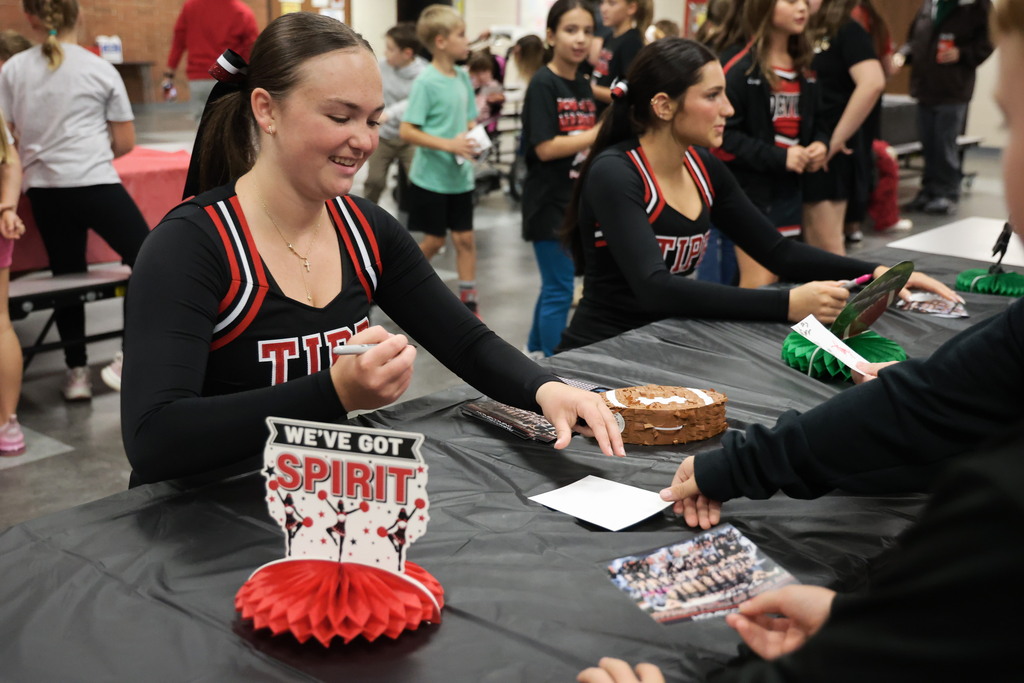 A cheerleader signs her autograph for a student.