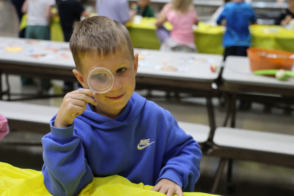 A student looks through a magnifying glass before looking closer at the inside flesh of a pumpkin.