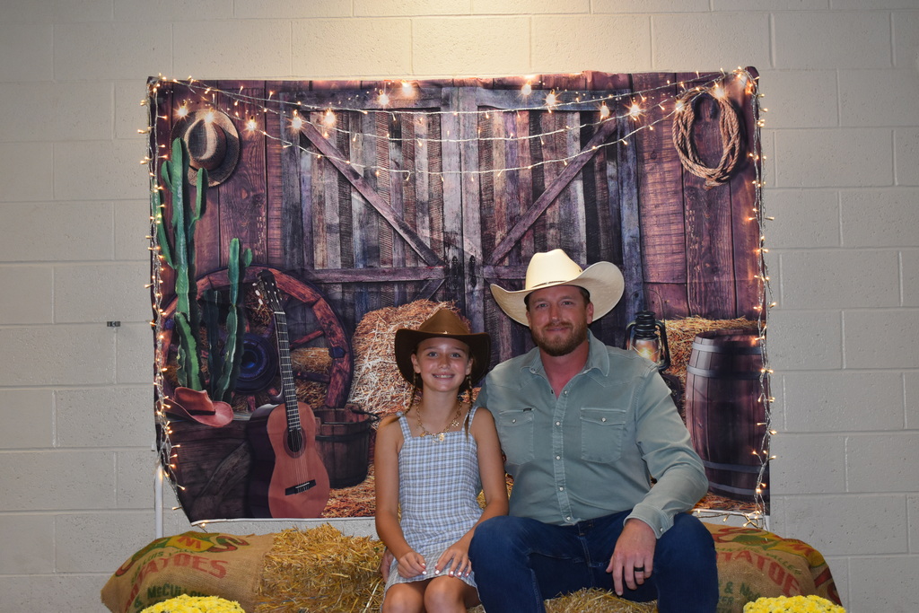 A father and his daughter pose for a photo at the hoe down.  