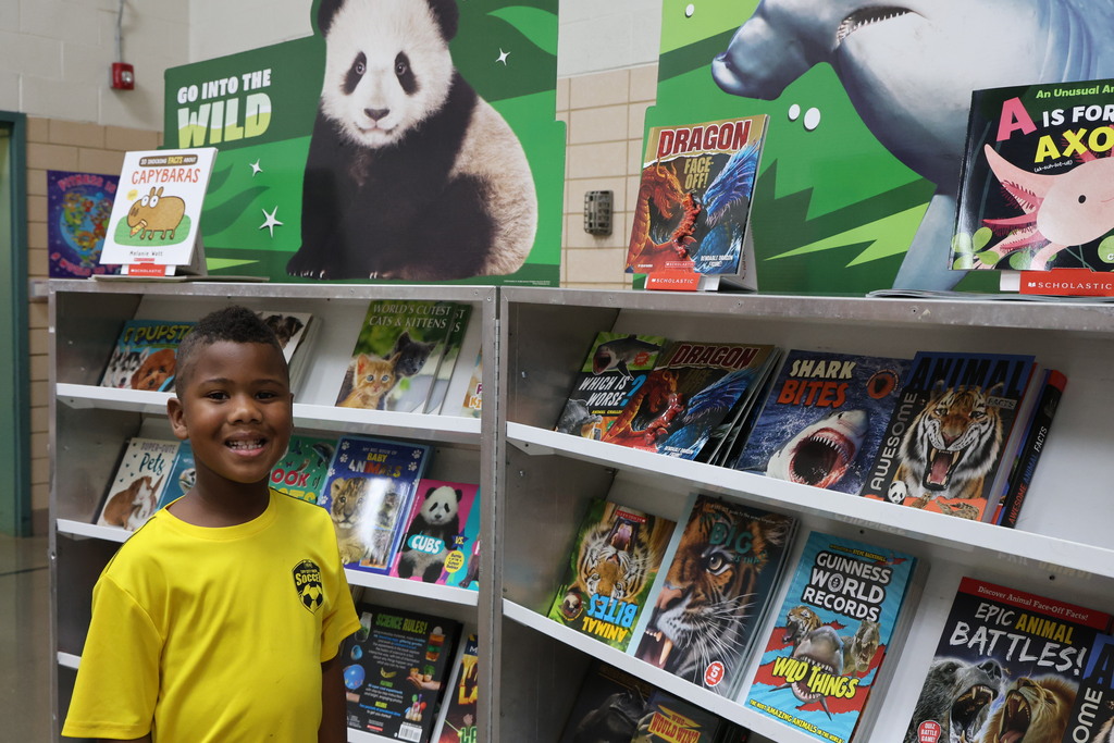 A student poses for a picture at the book fair before selecting some books.