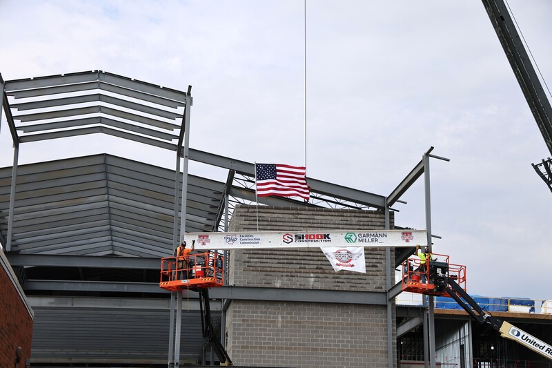 An American flag blows in the wind a top the beam being placed onto the new school.