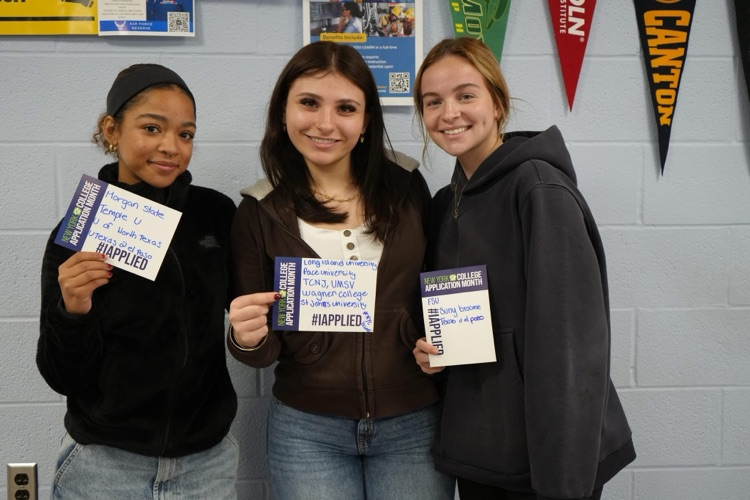 Three CTE students smiling holding #IAPPLIED cards with names of colleges on it