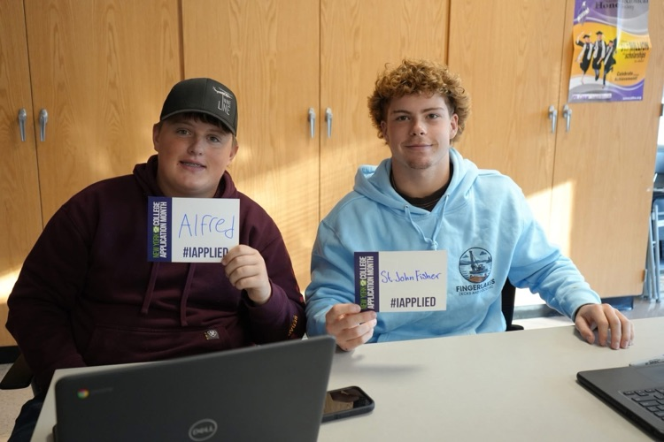 Two CTE students smiling holding #IAPPLIED cards with names of colleges on it