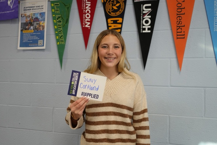 a student smiling holding #IAPPLIED card with names of colleges on it