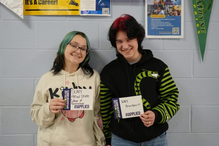 Two CTE students smiling holding #IAPPLIED cards with names of colleges on it