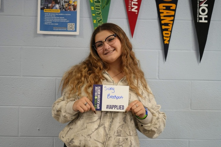 a student smiling holding #IAPPLIED card with names of colleges on it