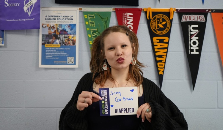 a student smiling holding #IAPPLIED card with names of colleges on it