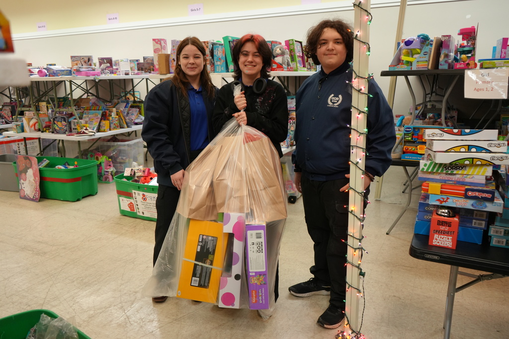 3 students posing for a picture with a bag of gifts
