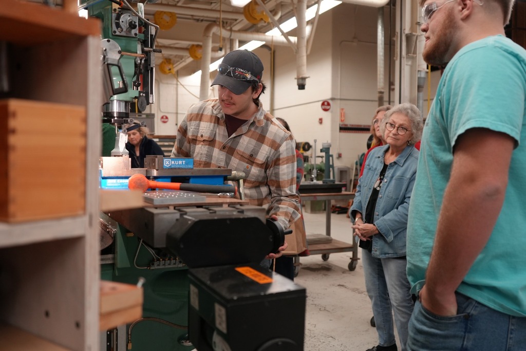A CTE Machining and Manufacturing student operates a milling machine while Board of Education members observe from nearby.