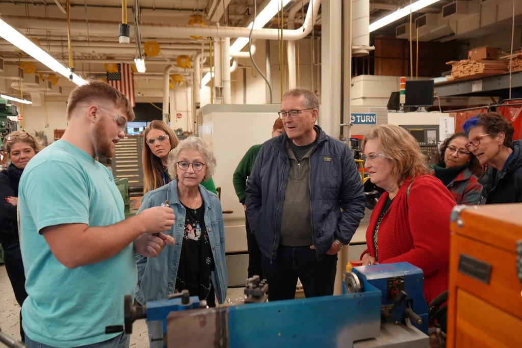 A CTE Machining and Manufacturing student explains a metalworking process to Board of Education members and administrators inside a machine shop.