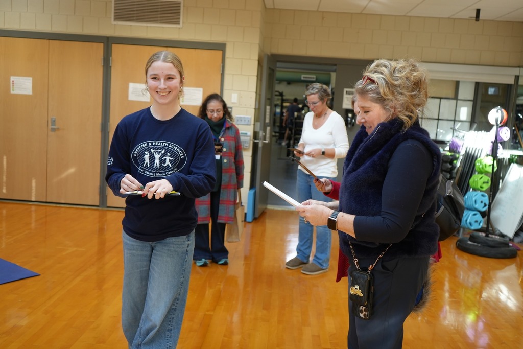 A New Visions Exercise and Health Sciences student explains an activity to Cindy Walter and other BOE members inside a fitness classroom while others observe.