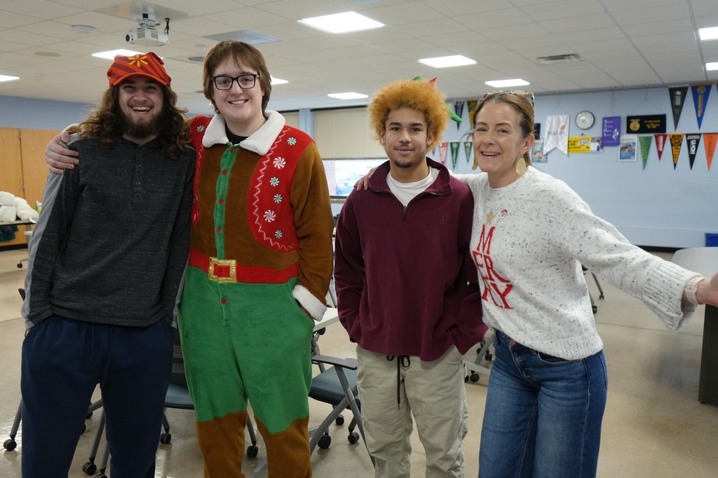 Students and a staff member stand together smiling inside career center, wearing festive holiday clothing during a campus celebration.