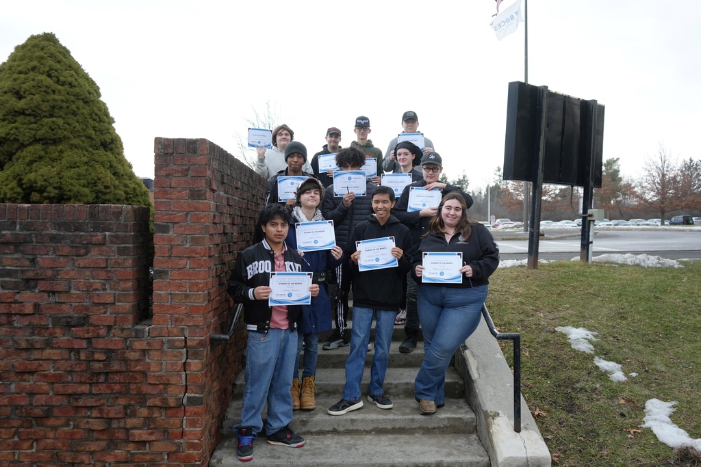 A group of CTE students stand on outdoor steps holding Student of the Month certificates in front of a brick building.