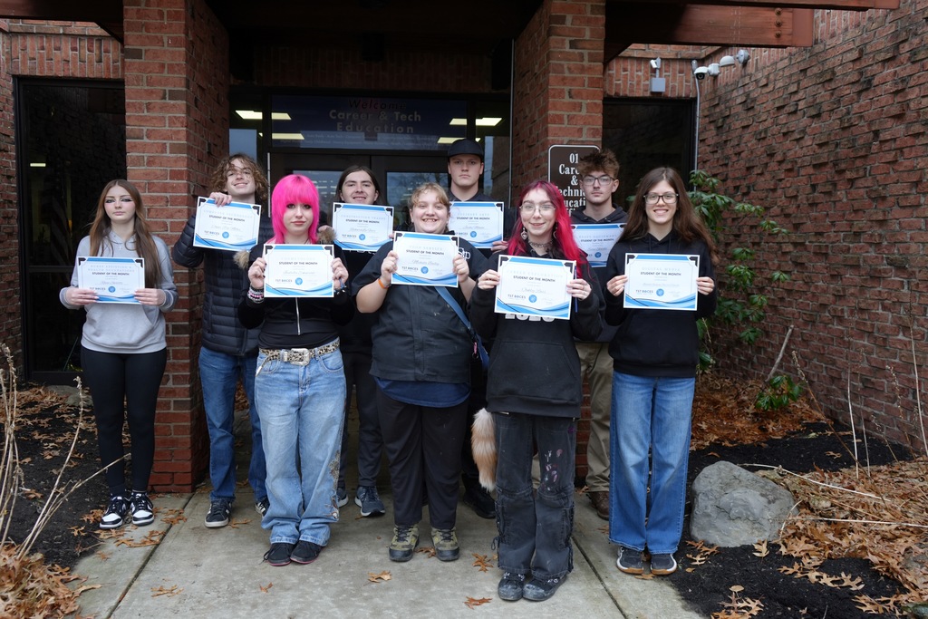 CTE students stand together outside the Career and Technical Education entrance, each holding a Student of the Month certificate.