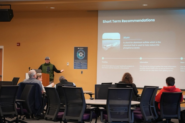 Student presenting at podium with slide about HABs