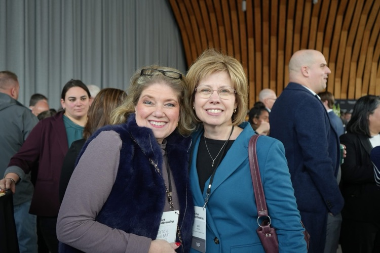 TST BOCES Assistant Superintendent Cindy Walter stands smiling with Tompkins Cortland Community College President Dr. Amy Kremenek amid a crowd of attendees at the Micron groundbreaking ceremony.