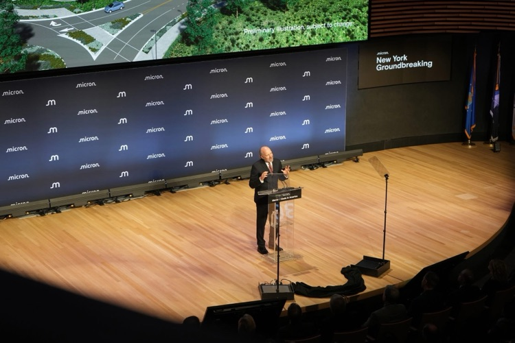 speaker at the podium on the Micron-branded stage, speaking to a seated audience during the groundbreaking event: Howard Lutnik
