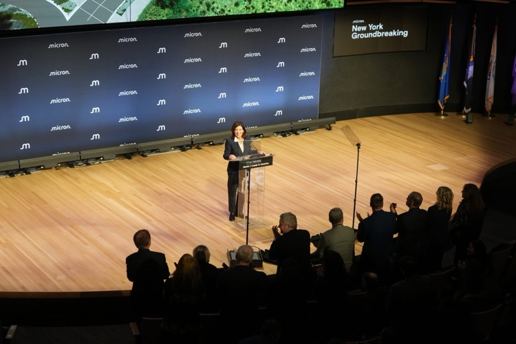 Governor Kathy Hochul smiles at the podium as audience members applaud during the Micron New York groundbreaking event.