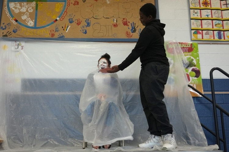 student smiles right after pier staff member sits in chair with shipped cream all over their face