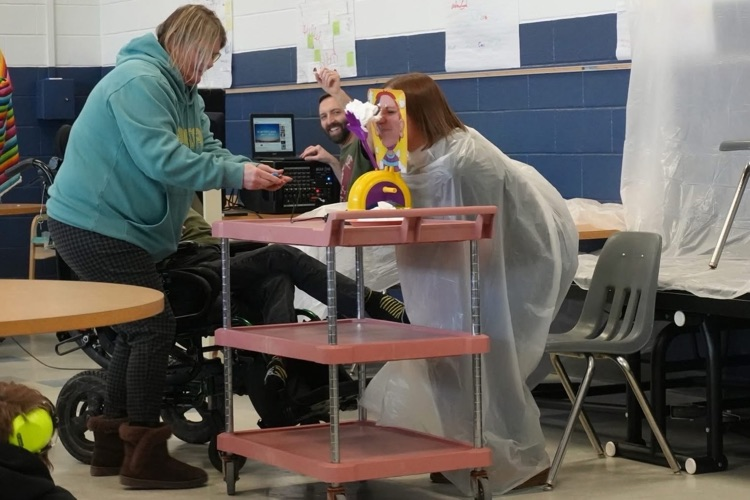 staff member puts head through pie in the face contraption just as whipped cream gets closer and closer in game to her face