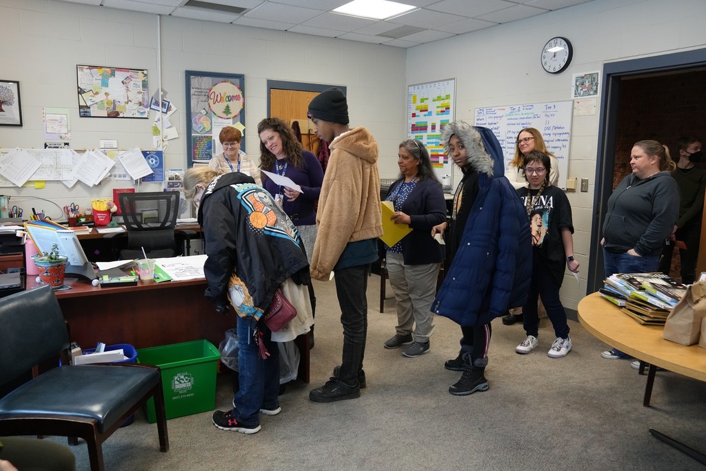 Board members and staff observe as students line up in an office to sign a recognition poster during the High Five ceremony at Smith School.