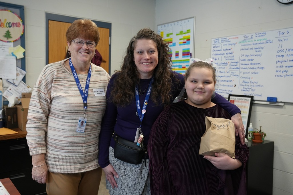 A student stands smiling beside Princpal Adams and BOE Member AnnMarie Streeter while holding a small congratulatory prize bag during the High Five recognition ceremony.