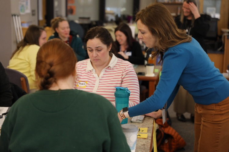  A facilitator leans in to support a small group of educators working together at a table during a hands-on activity.