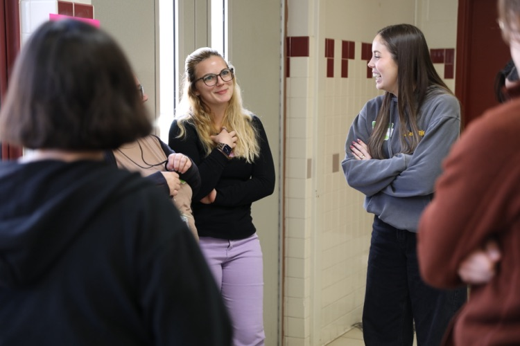 Two educators stand in a hallway, smiling and chatting with colleagues during a small group session in the professional development day.