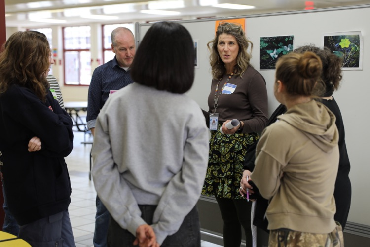  A facilitator leads a small group discussion with educators standing in a hallway, engaging in conversation and collaboration.